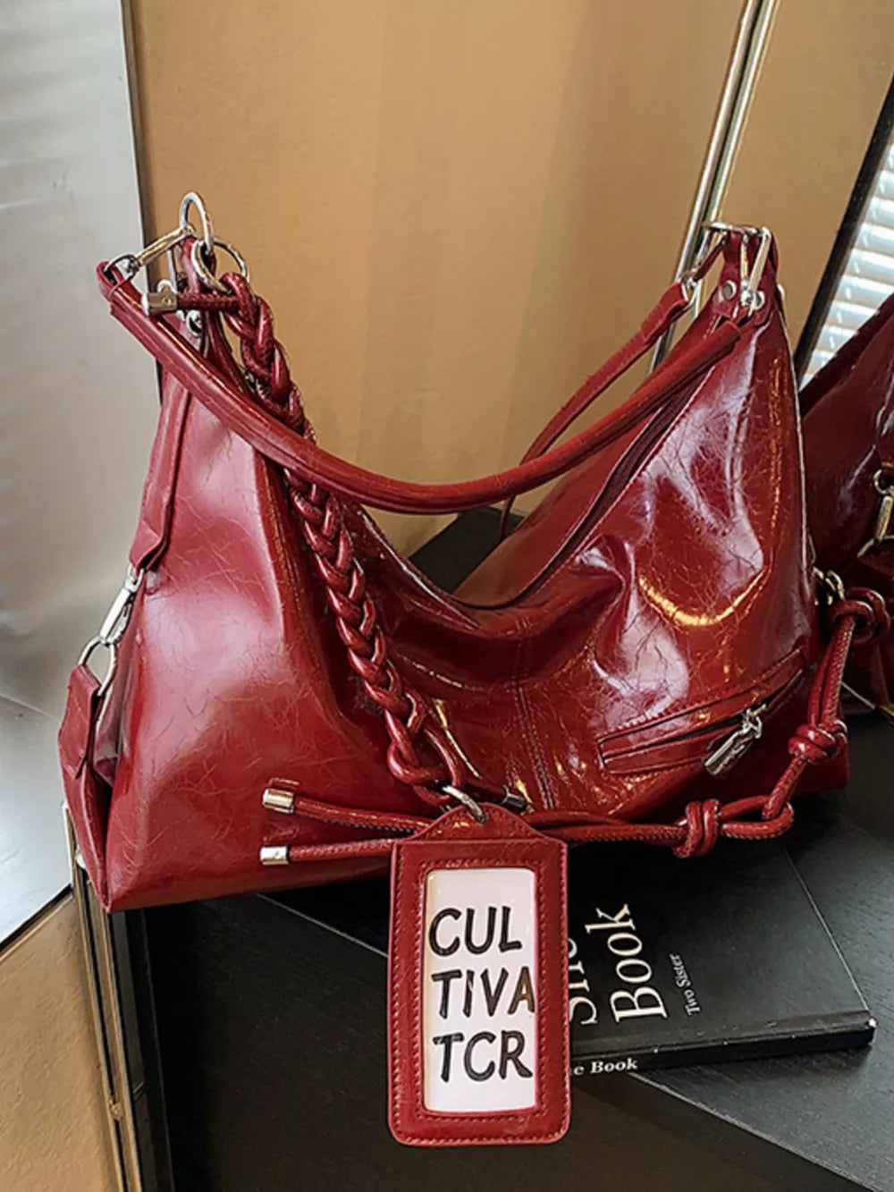 Red vintage-inspired shoulder bag with braided strap detail and luggage tag.