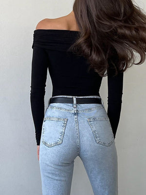 Black off-shoulder long sleeve bodysuit with ruching detail, worn with light wash jeans and a black belt.