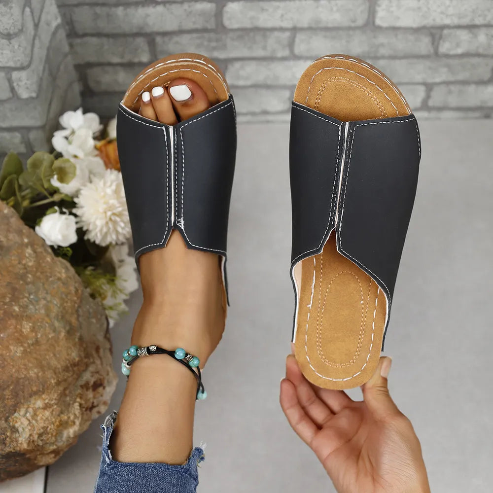 Black vegan leather asymmetrical slides with white stitching detail.