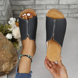 Black vegan leather asymmetrical slides with white stitching detail.