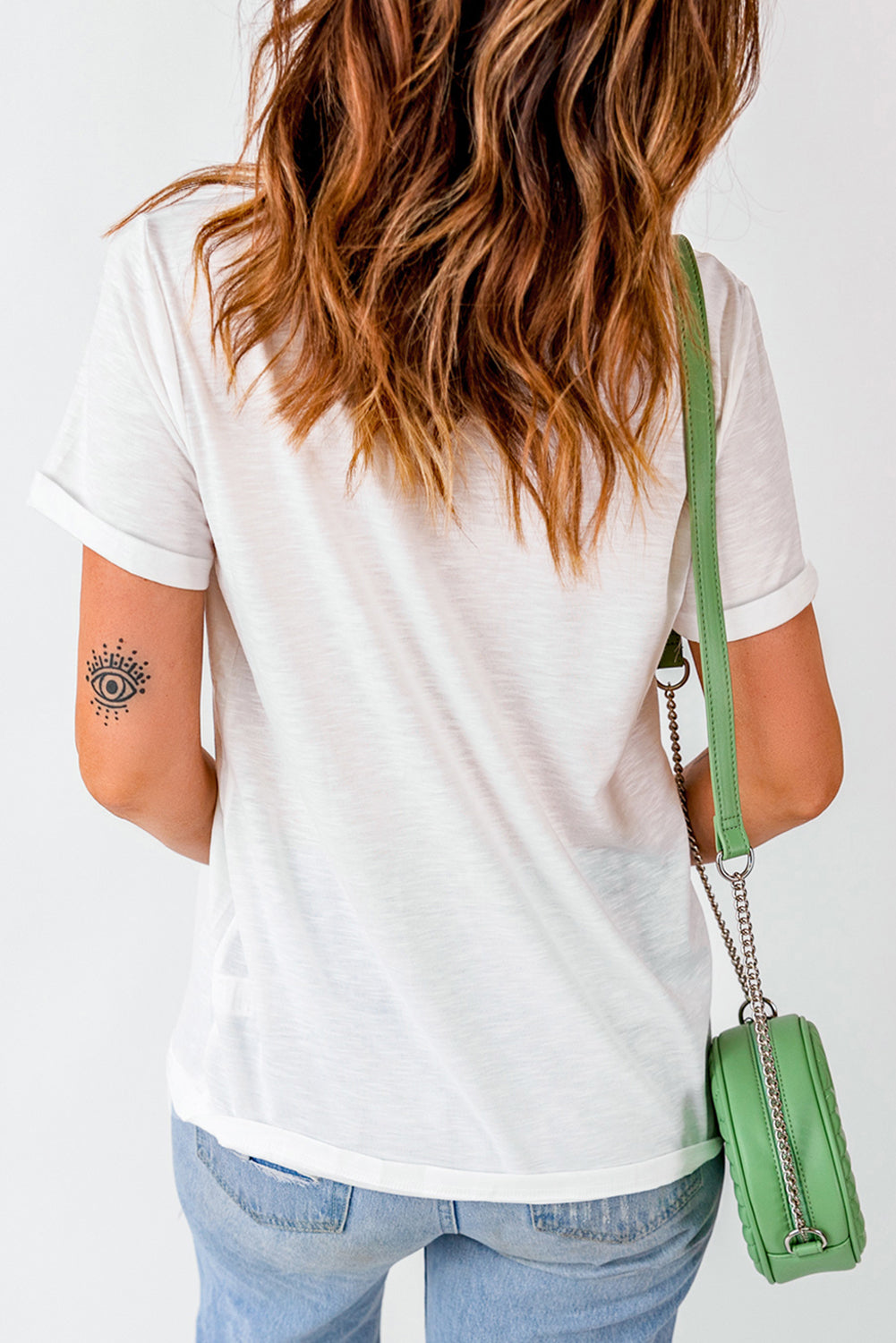White t-shirt with rolled sleeves and an eye tattoo on the arm.