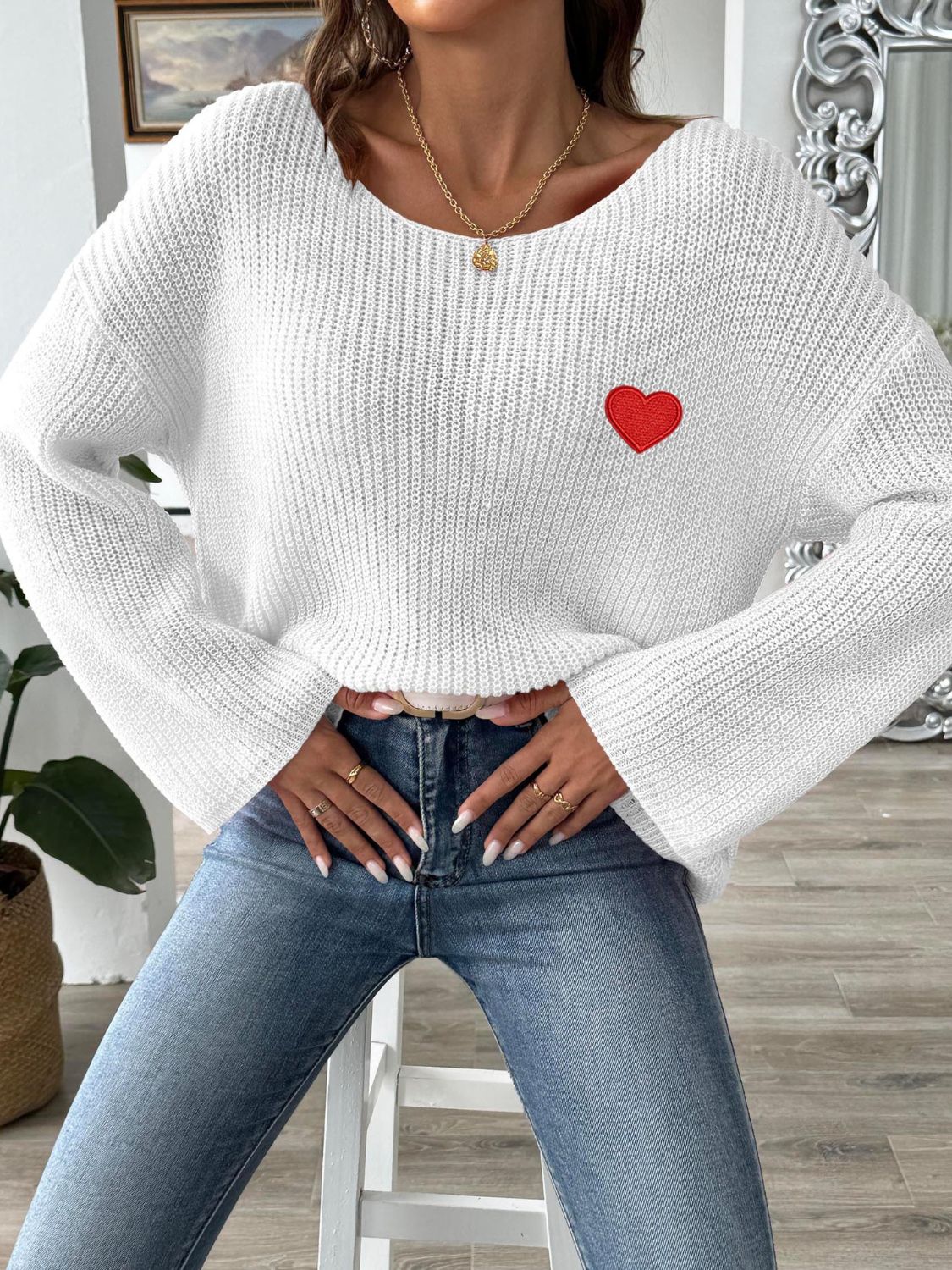 White knit boatneck sweater with embroidered red heart detail.