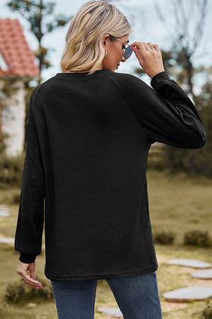Black waffle knit eyelet raglan sleeve top with textured sleeves and crew neck.