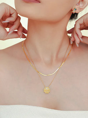Gold layered necklace with a dainty clover charm and a flat herringbone chain.
