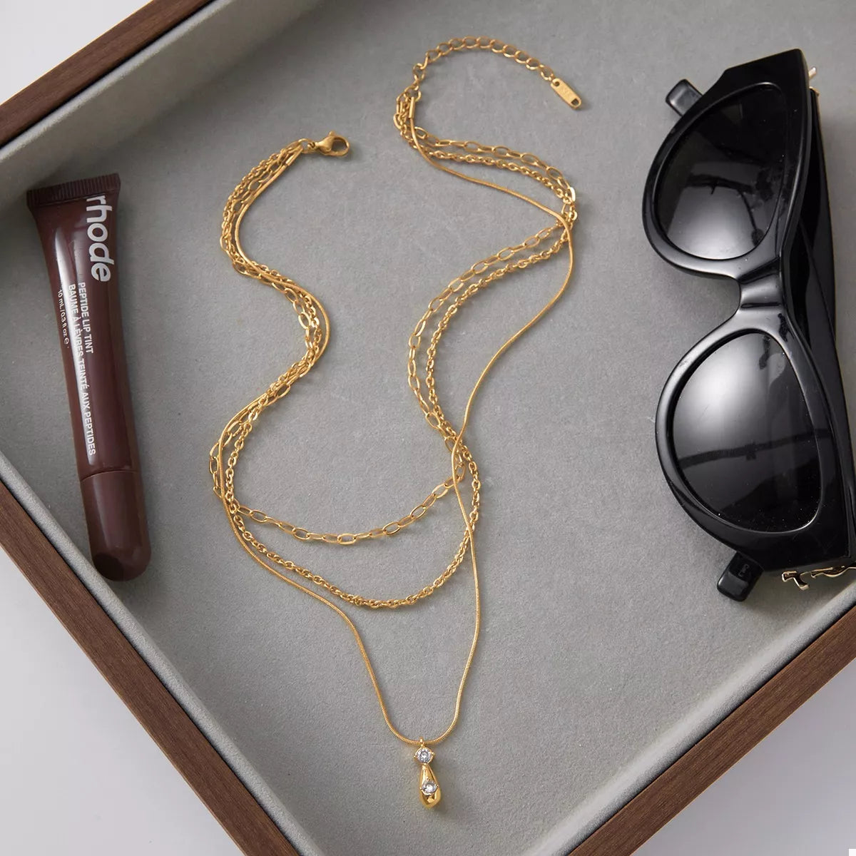 Gold three layered pendant necklace with a teardrop charm and two small crystals.