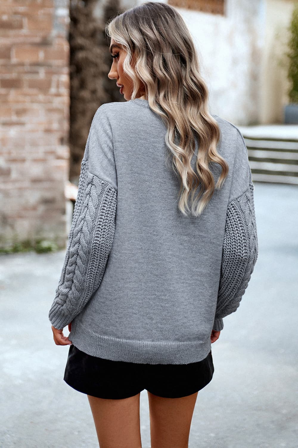Light gray acrylic sweater with cable-knit sleeves and relaxed fit.