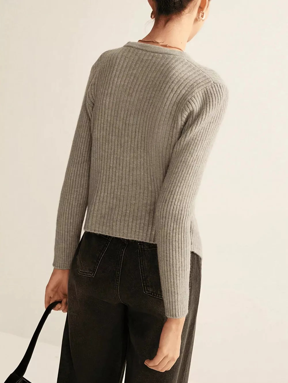Grey ribbed knit cardigan with crew neck and asymmetrical hem, styled with dark wash jeans.