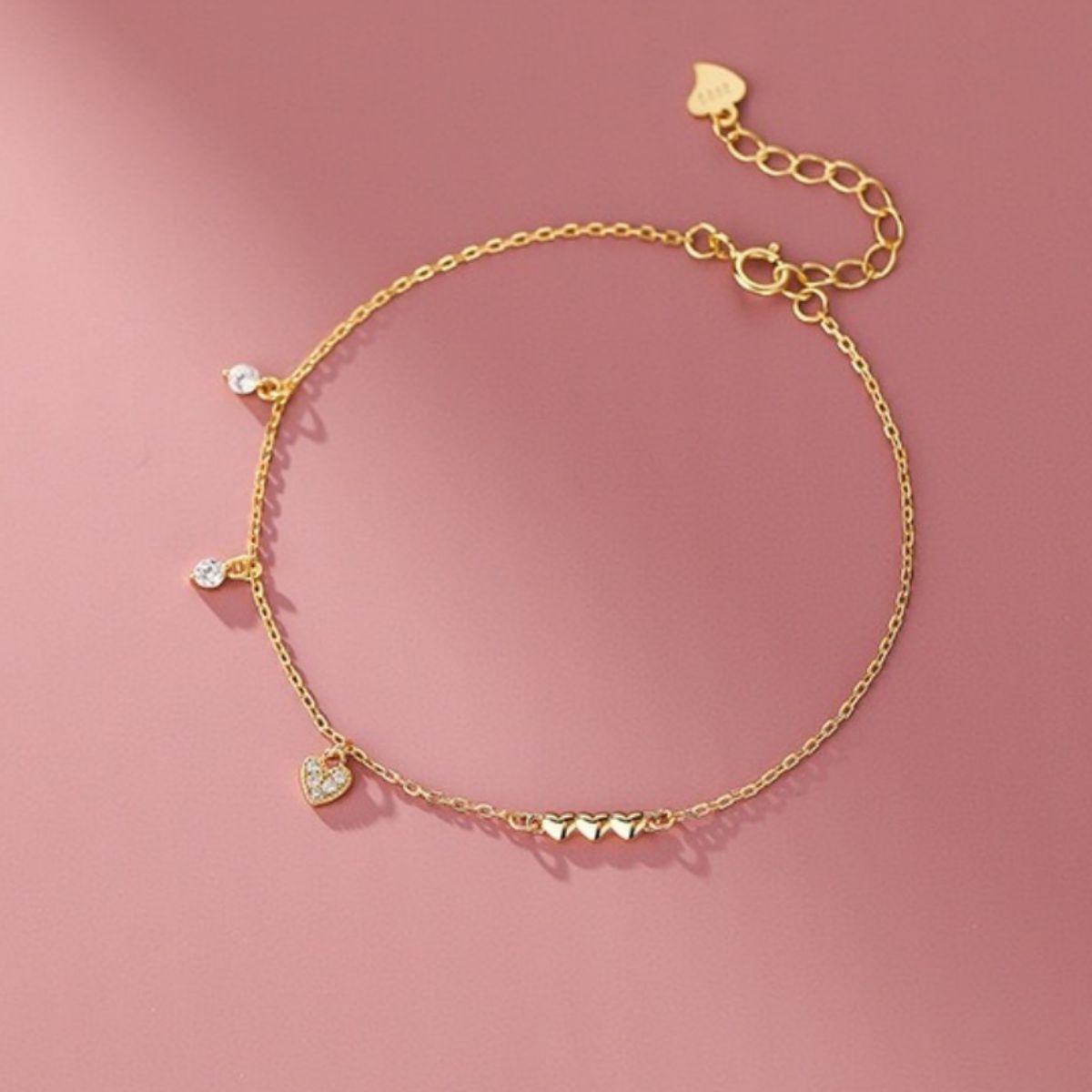 Gold pavé heart charm bracelet with cubic zirconia accents and three small heart charms.