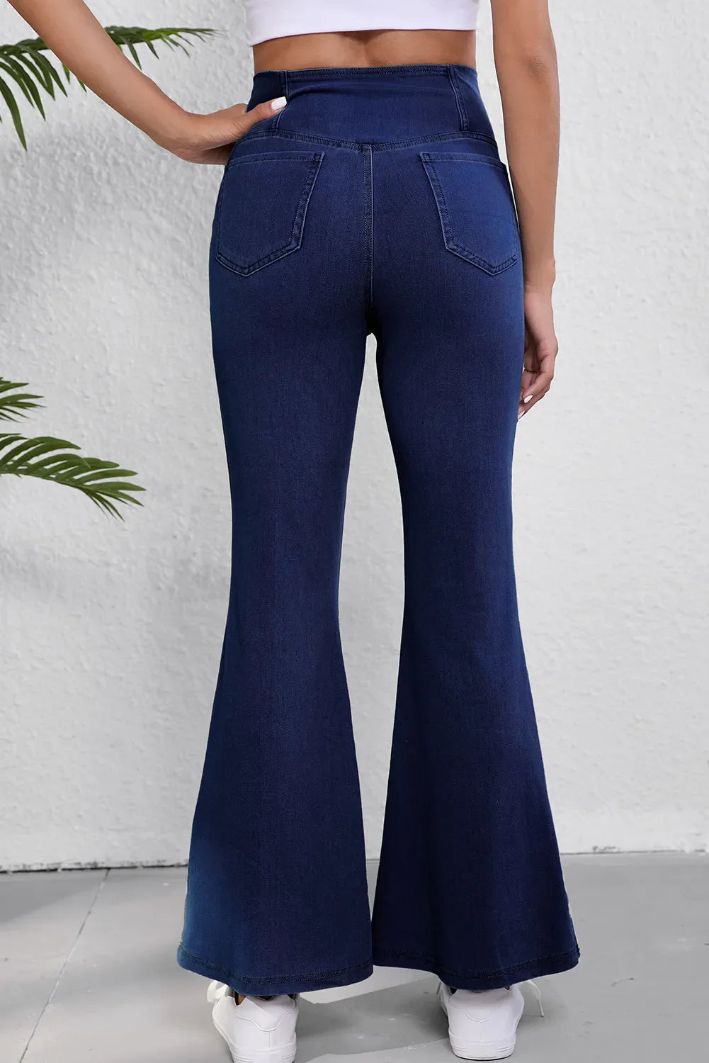 Crossover waist denim flare trousers in medium wash, showing back pockets and flared leg opening.