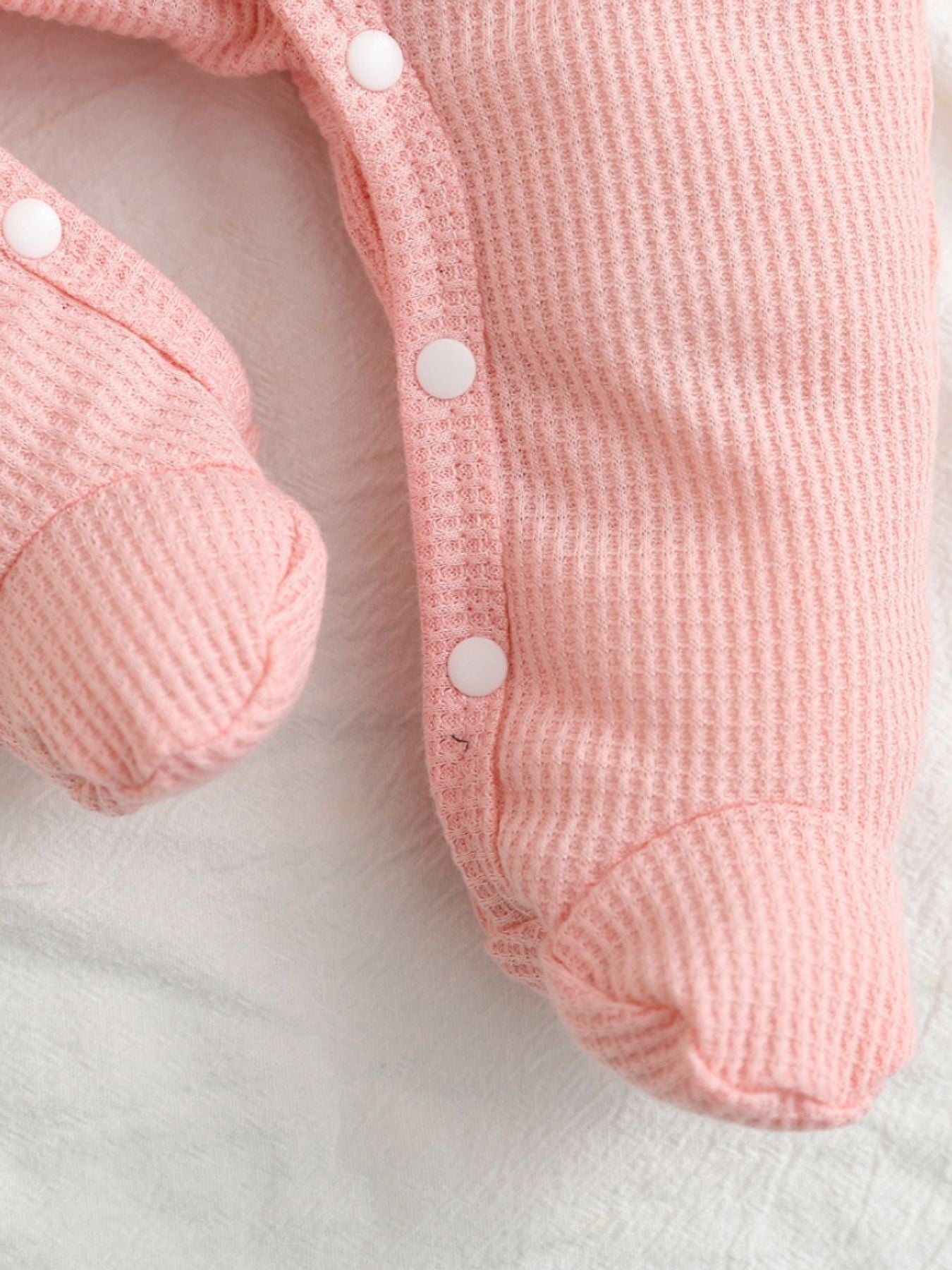 Blush pink waffle knit baby one-piece with white snap buttons and footies