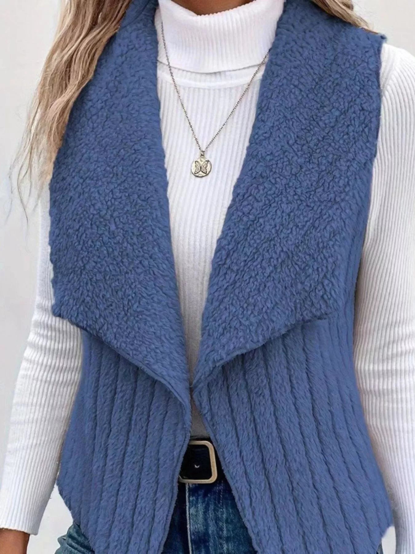 Blue fleece vest with open front and ribbed texture, worn over a white turtleneck.