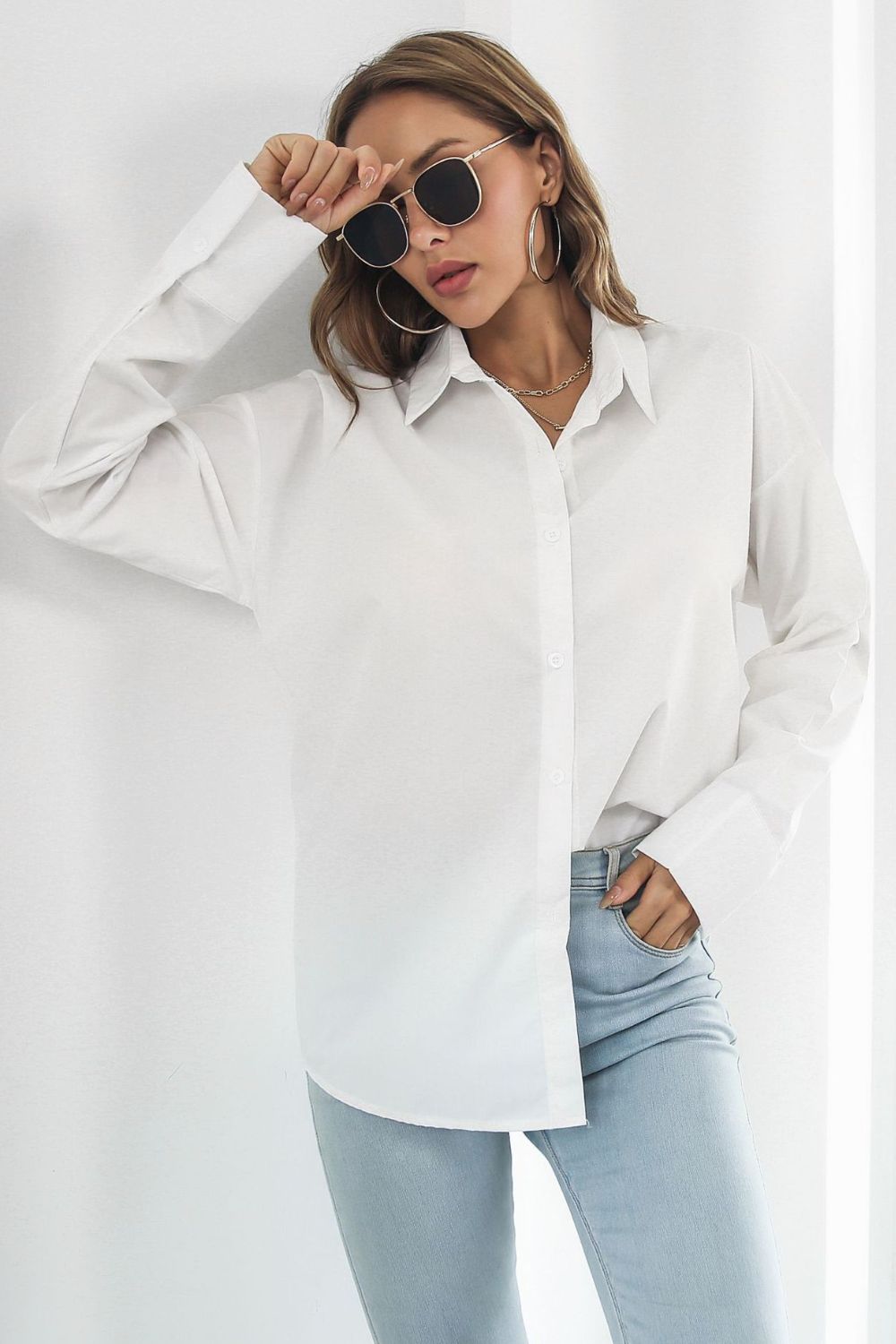 Oversized white cotton poplin shirt with button front and long sleeves styled with jeans.