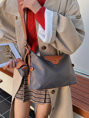 Gray canvas hobo bag with coin purse and tan trim, worn with a trench coat.