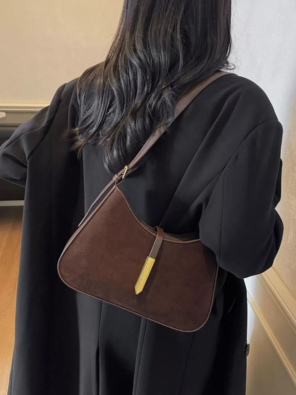 Curved coffee brown suede shoulder bag with leather trim and gold accent.