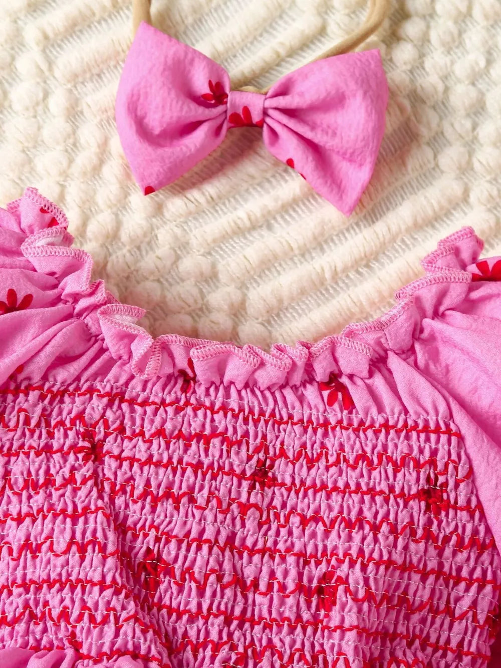 Pink floral smocked baby dress with ruffled neckline and matching bow headband.
