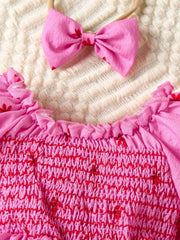 Pink floral smocked baby dress with ruffled neckline and matching bow headband.