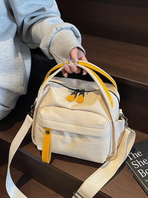 Cream canvas crossbody bag with yellow accents and decorative pull tab.
