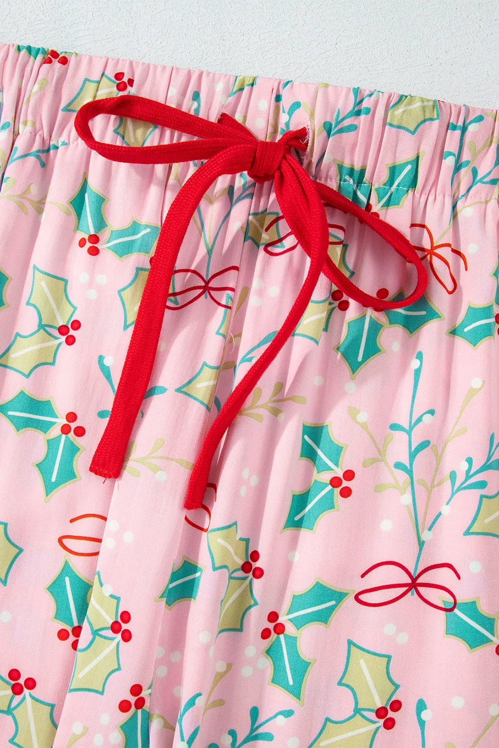 Blush pink pajama pants with holly print and red drawstring.