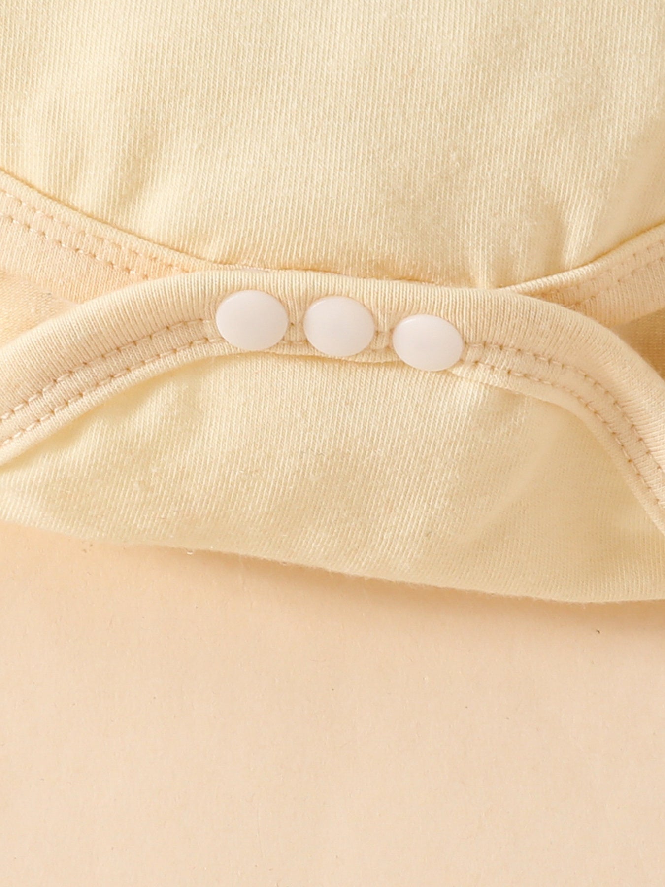Baby bodysuit detail with three white snaps and ruffled trim in pale yellow cotton.