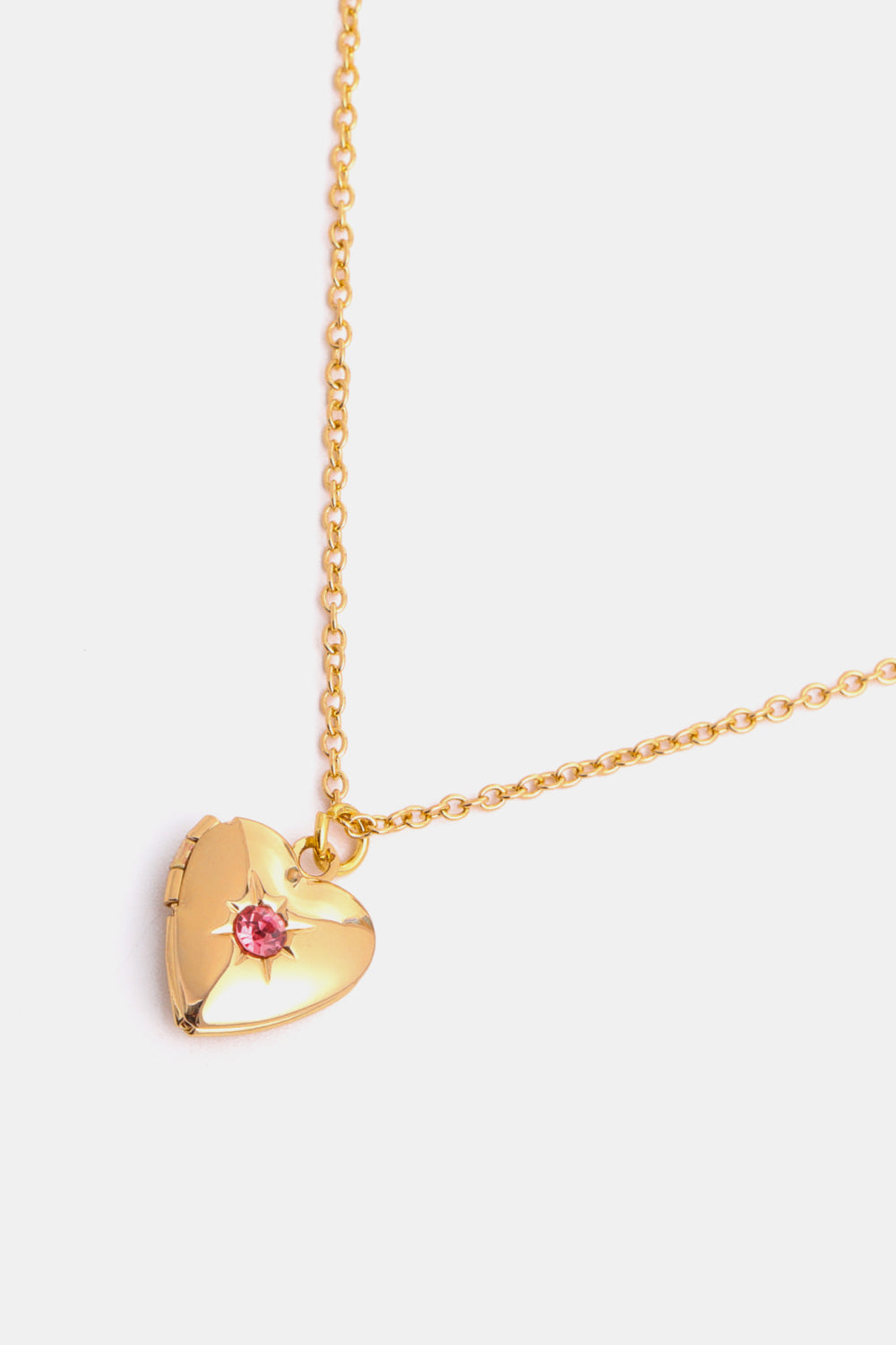 Gold heart locket necklace with pink gemstone and starburst detail on a delicate chain.