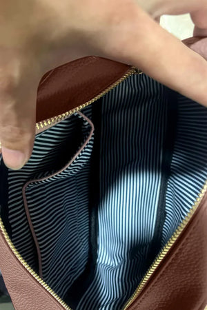 Textured crossbody bag interior with striped lining and pink trim pocket.
