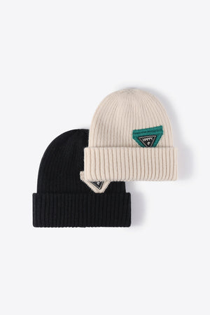 Ribbed acrylic beanies in black and beige, each with a green triangular patch detail.