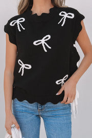 Black knit vest with white bow print, scalloped hem, and ruffled neckline.