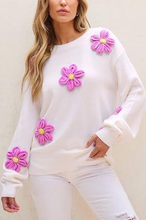 White knit sweater with pink embroidered flower details and yellow centers.