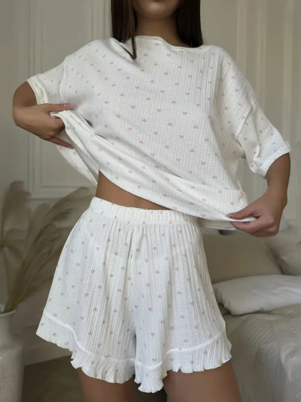 White cotton blend pajama set with pink heart print, featuring a relaxed fit tee and ruffled shorts.