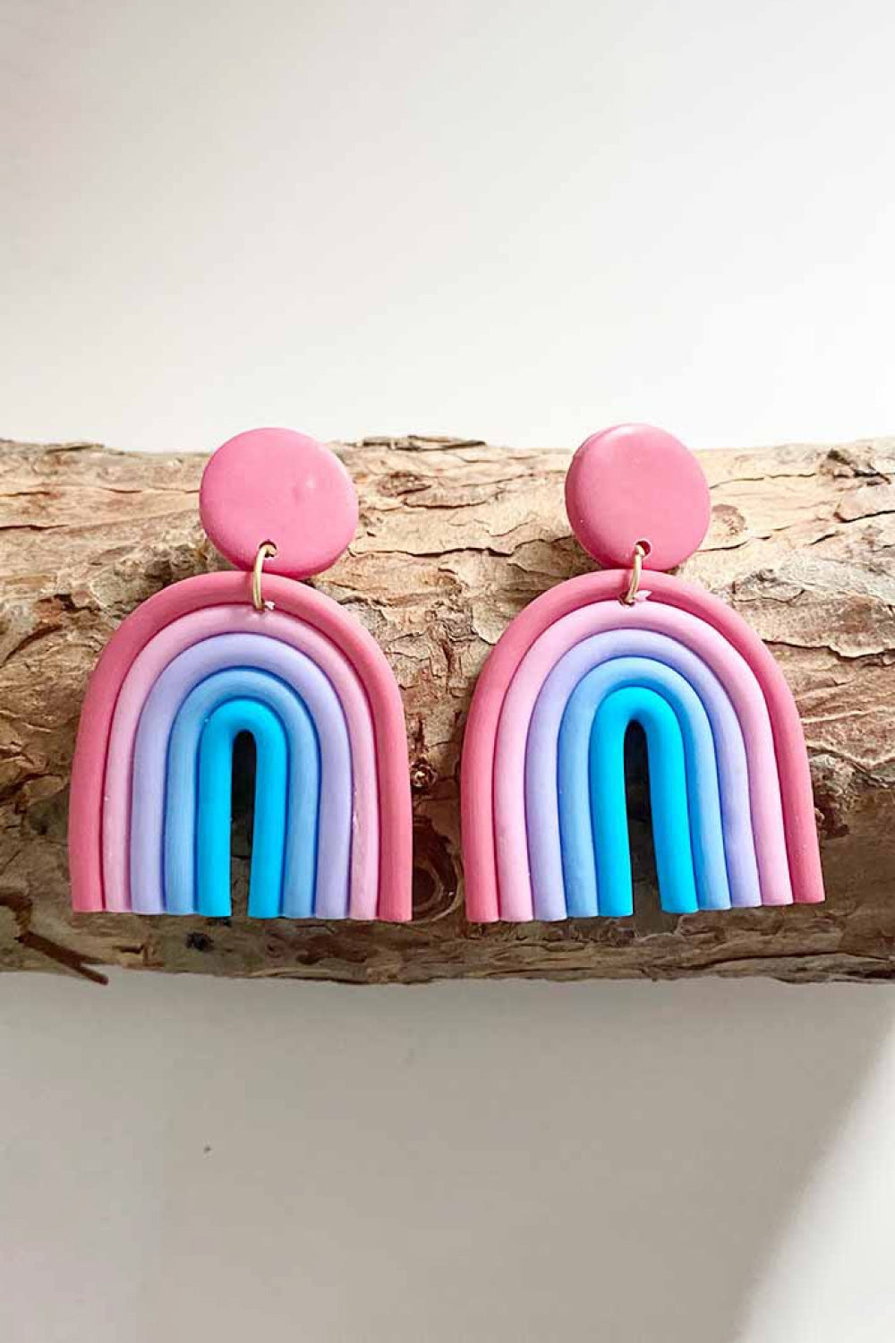 Rainbow arch clay earrings in pink, lavender, and aqua with a pink stud.