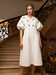 White midi dress with puff sleeves, V-neck, and rhinestone embellishments.