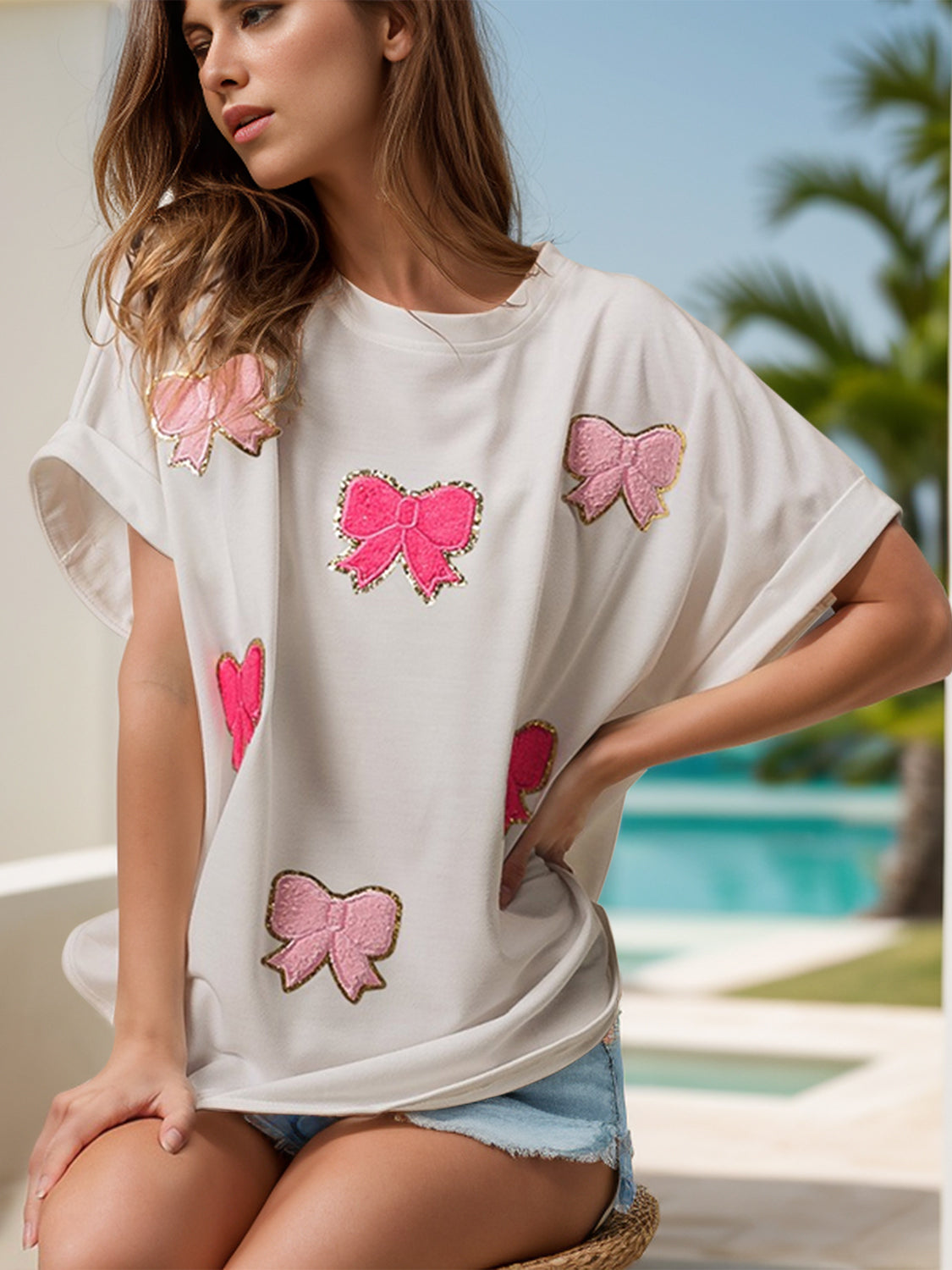 White oversized tee with pink sequin bow embellishments and rolled sleeves.