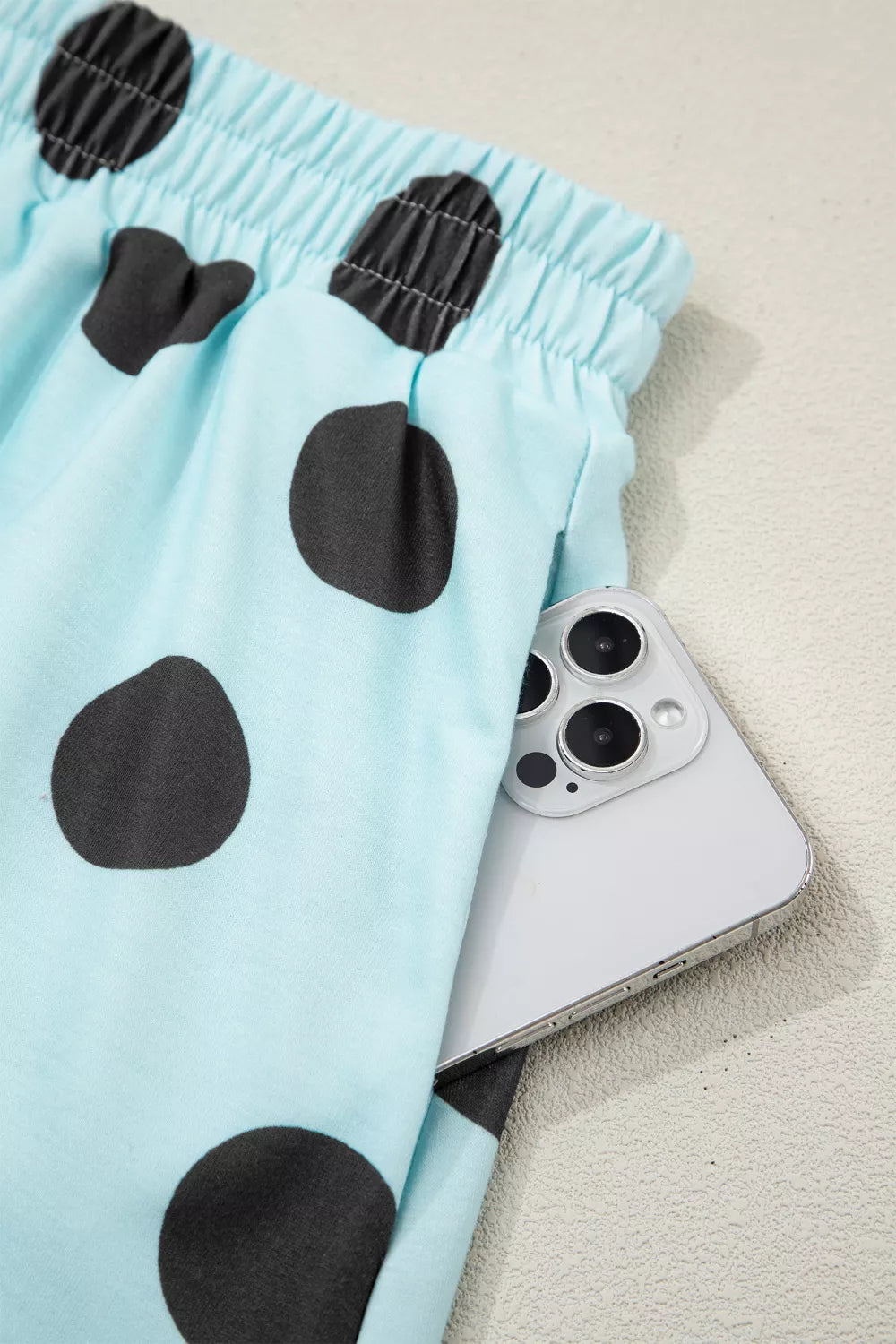 Light blue polka dot shorts with elastic waist and side pocket holding a phone.