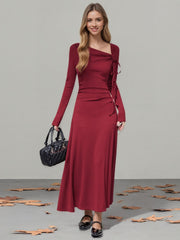 Burgundy long-sleeve maxi dress with asymmetrical neckline and tie detail.