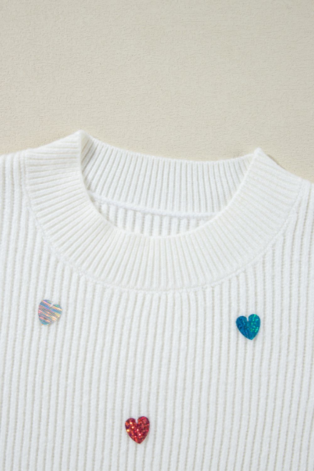 White ribbed knit sweater with scattered heart embellishments.