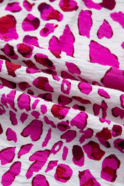 Vibrant leopard print V-neck blouse with pink and red spots on white fabric.