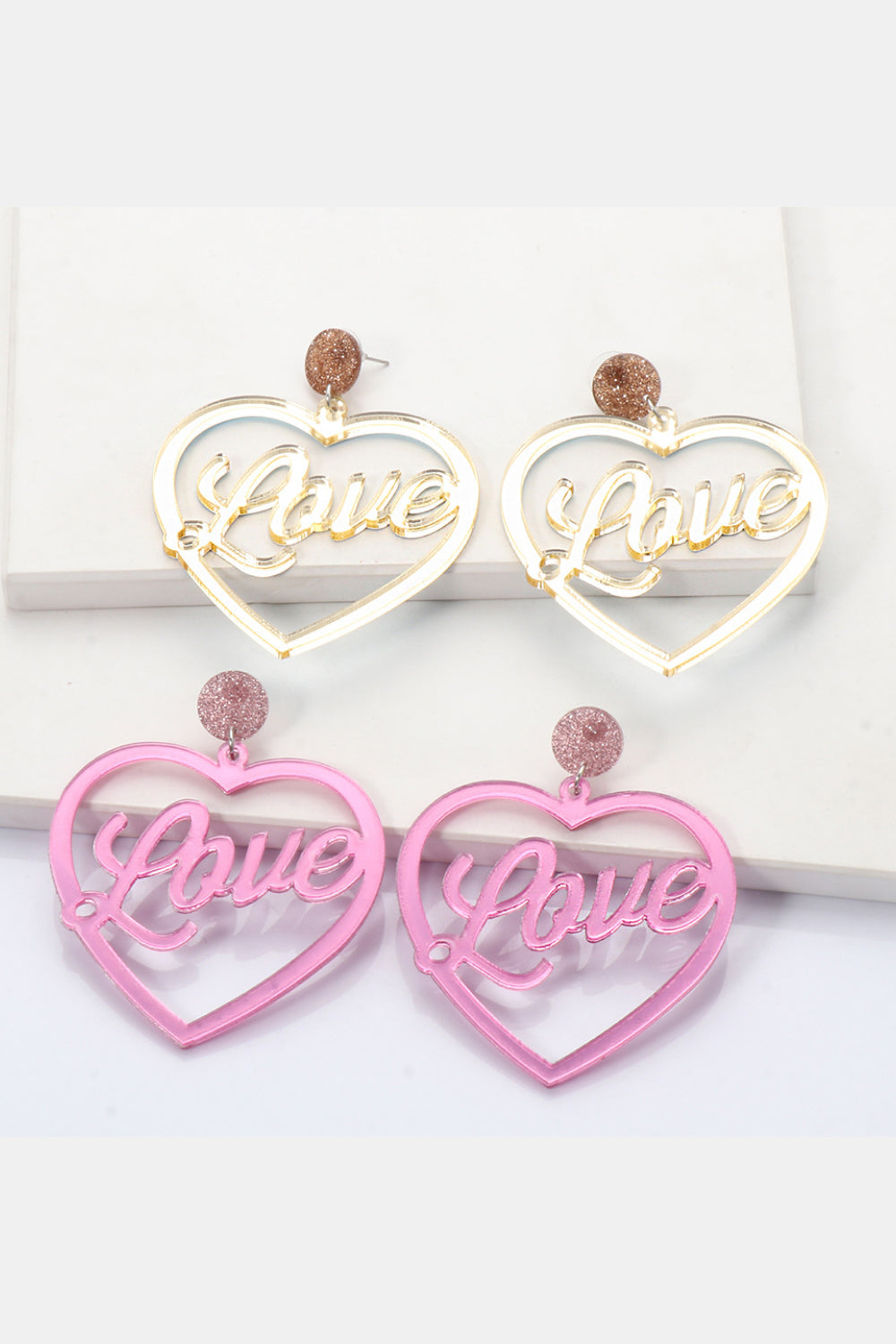 Glitter studded acrylic heart earrings with "Love" cutout in pink and gold.