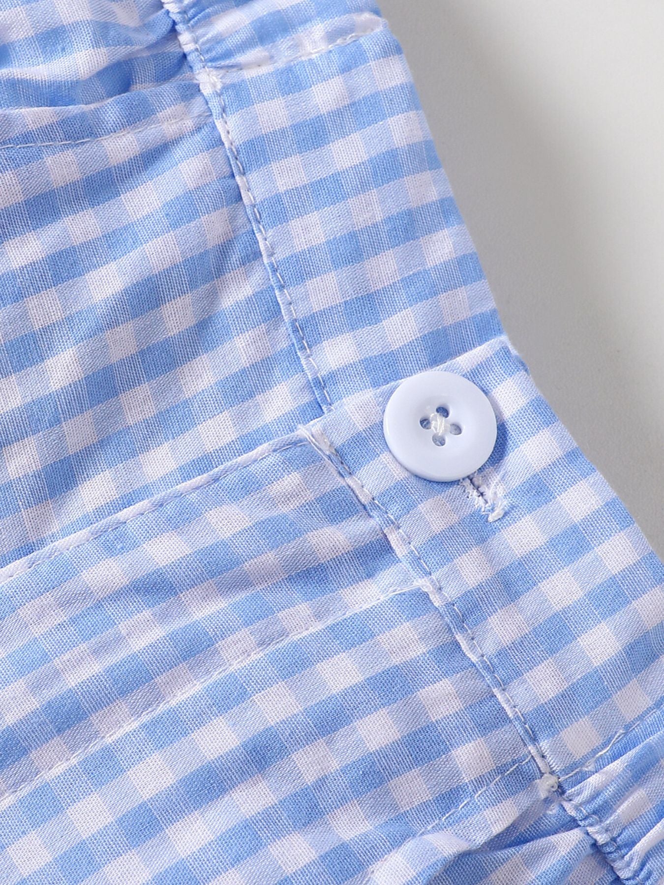 Blue gingham baby shorts with a white button detail and pocket.