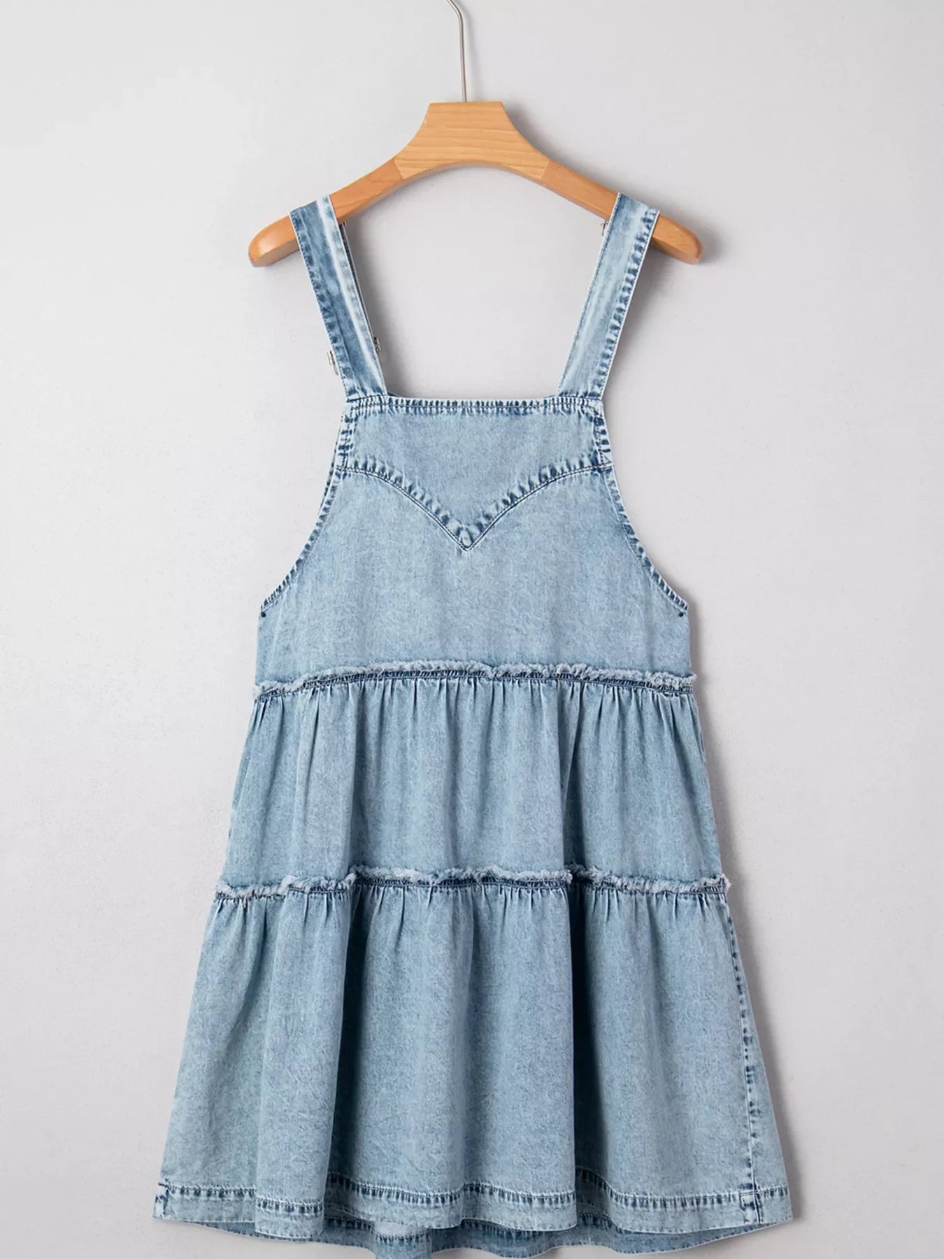 Tiered denim overall dress in light blue with ruffled tiers and V-neck bodice.