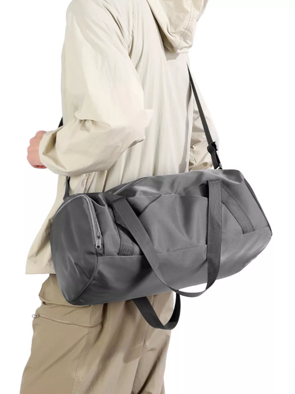 Gray barrel duffle bag with zippered pocket and shoulder strap, worn by a person.