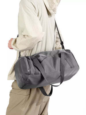 Gray barrel duffle bag with zippered pocket and shoulder strap, worn by a person.
