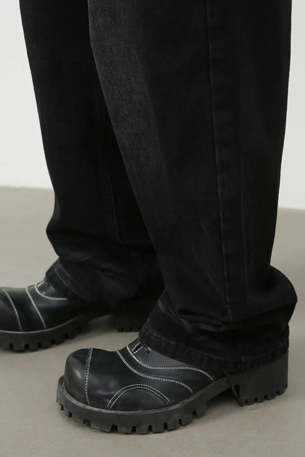 Faded black baggy denim trousers with white contrast stitching on black platform boots.