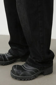 Faded black baggy denim trousers with white contrast stitching on black platform boots.