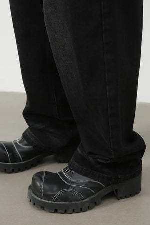 Faded black baggy denim trousers with white contrast stitching on black platform boots.