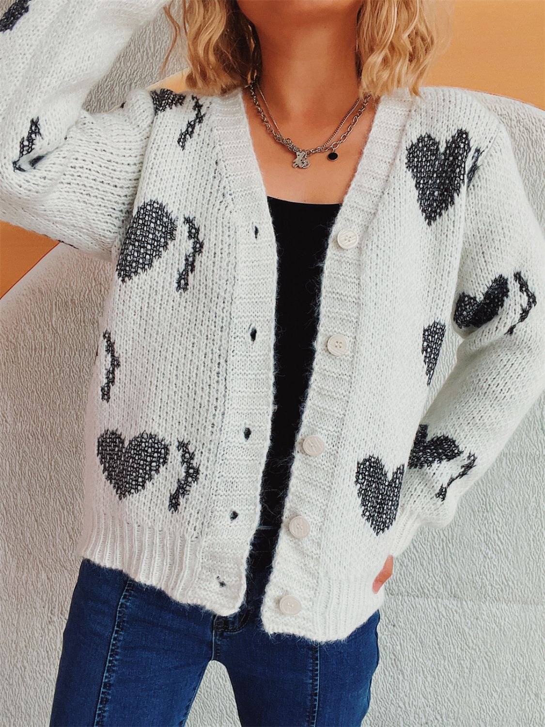 White knit cardigan with black heart motif, button front, V-neck, long sleeves.