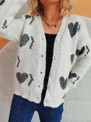 White knit cardigan with black heart motif, button front, V-neck, long sleeves.