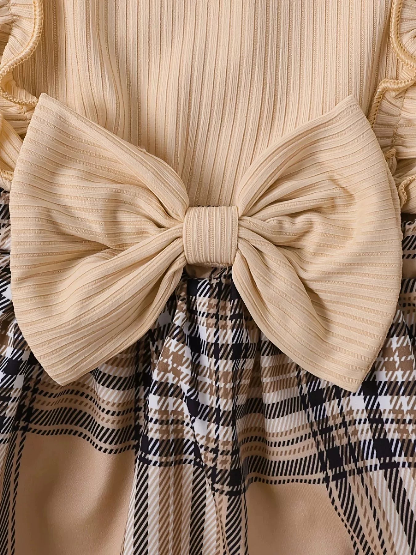 Baby bodysuit with ruffled trim and large bow, paired with a plaid skirt.
