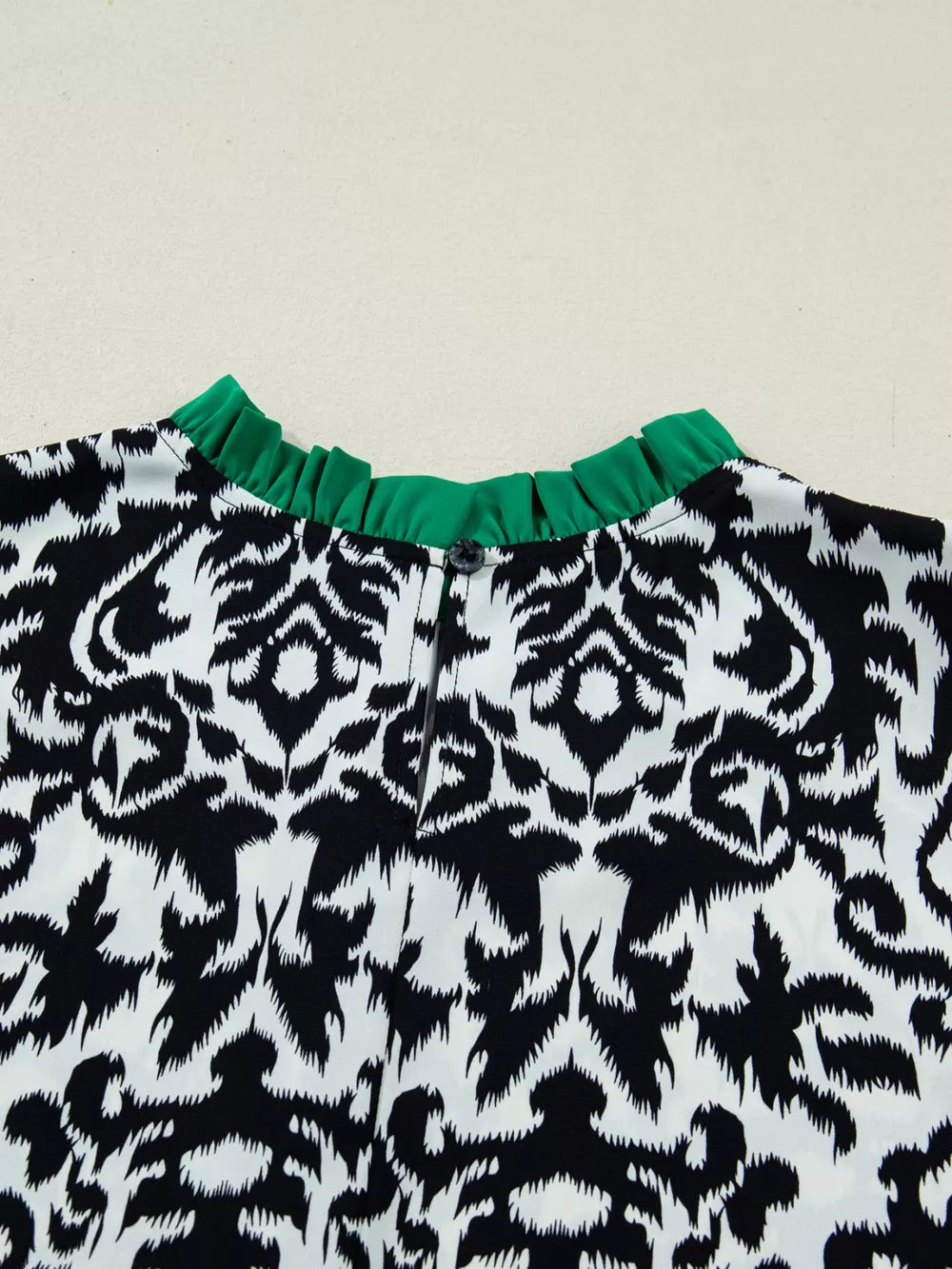 Maternity blouse with damask print, ruffled green neckline, and button detail.