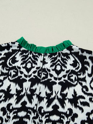 Maternity blouse with damask print, ruffled green neckline, and button detail.