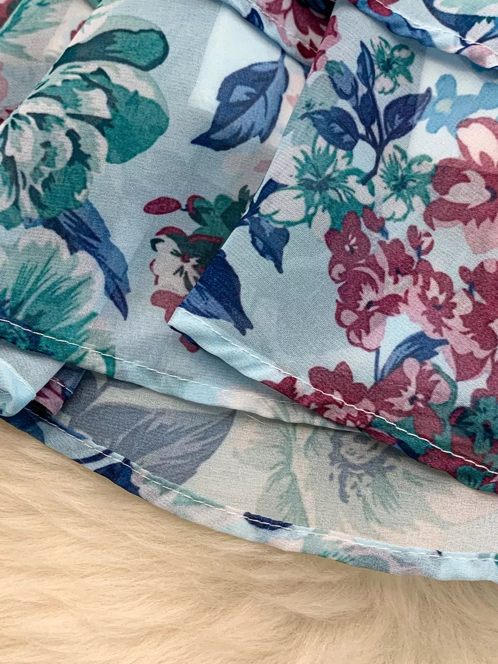 Light blue floral ruffle hem wrap mini dress detail with white stitching.